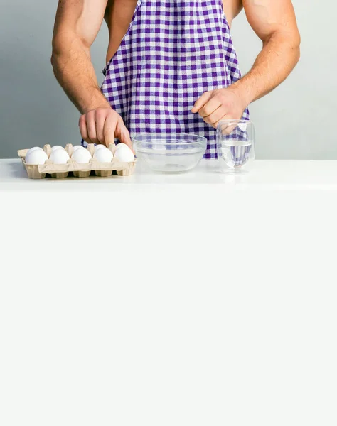 厨师健美者穿着防护围裙 在白色厨房桌子上煮鸡蛋 肌肉男做饭 健康食品和节食 运动员的食品添加剂 每日卡路里饮食 — 图库照片