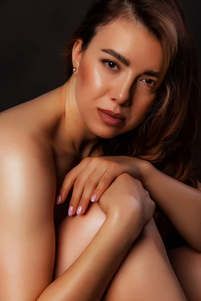 Close up portrait side view nude woman sitting on the floor on black studio background. Beauty and skin care concept.