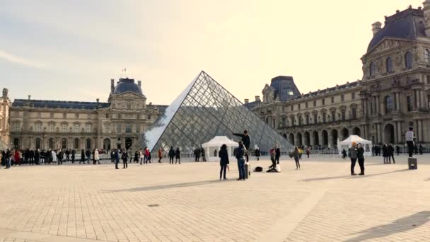 ルーヴル美術館の前にある三角形のガラスのピラミッド フランスのパリのルーブル美術館 日中はルーブル美術館の前を歩く人々 — ストック動画