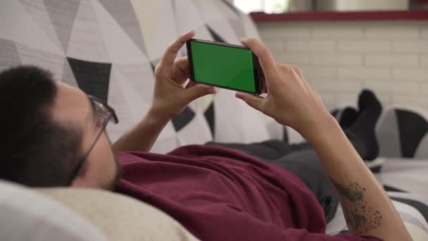 Молодий Чоловік Лежить Дивані Дивиться Свій Мобільний Телефон Зелений Екран — стокове відео