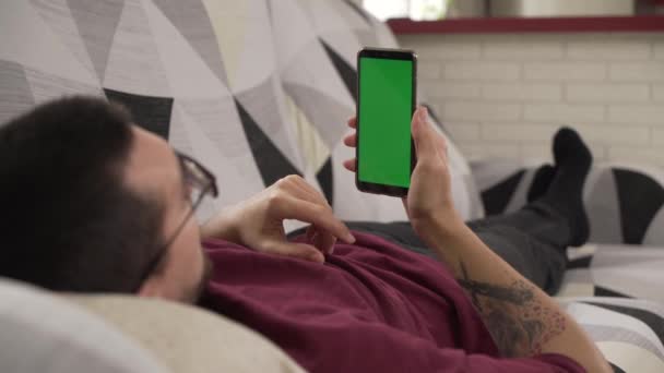 Joven Acostado Sofá Mirando Teléfono Celular Pantalla Verde — Vídeos de Stock