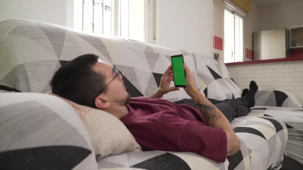 Joven Acostado Sofá Mirando Teléfono Celular Pantalla Verde — Vídeos de Stock