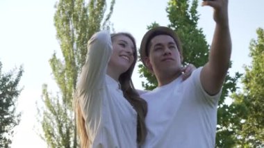 Parkta cep telefonlarından selfie çeken genç bir çift. Latin erkek ve beyaz kadın.