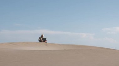 Adam çölde dizüstü bilgisayarla çalışıyor. Dijital göçebe ve uzaktan çalışan kavramı