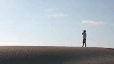 Çöldeki kum tepelerinde akıllı bir telefonla arayan bir adam. Boşluğu kopyala