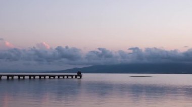 Tanınmayan insanlar yazın gün batımında deniz kenarında iskelede dinleniyorlar.