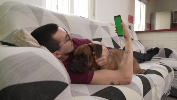 Молодий Чоловік Своєю Собакою Лежить Дивані Дивиться Свій Мобільний Телефон — стокове відео