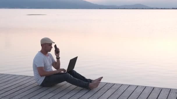 Άντρας Ταξιδιώτης Κάθεται Στην Ακτή Χρησιμοποιώντας Φορητό Υπολογιστή Και Smartphone — Αρχείο Βίντεο