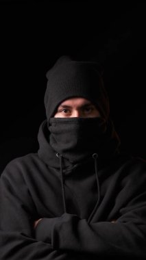 Siyah kar maskeli bir hırsız ve siyah şapkalı bir adam kameraya dik dik bakıyor.