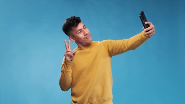 Homem enviando um beijo de ar e fazendo poses e rostos ao tirar selfies com seu telefone celular. — Vídeo de Stock