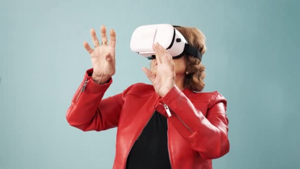 Femme âgée expérimentant la réalité virtuelle avec des lunettes VR tout en se tenant sur un fond isolé. — Video
