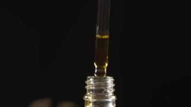 Dropper dripping cannabis CBD oil over a dark background.