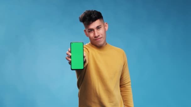 Чоловік Вказує Смартфон Зеленим Екраном Стоячи Синьому Фоні Повільне Відео — стокове відео