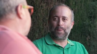 Orta yaşlı erkek, yaz günü arka planda bulanık bir şekilde sokakta otururken ekinlere bakan isimsiz bir arkadaşa bakıyor.