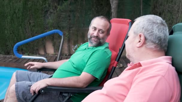 Δύο Άνδρες Χαλαρώνουν Καθισμένοι Καρέκλες Έναν Κήπο Κοντά Μια Πισίνα — Αρχείο Βίντεο