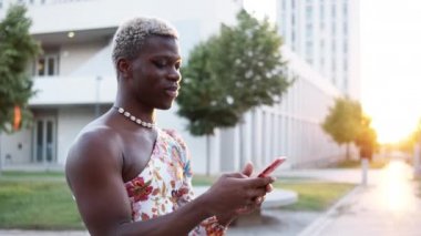 Afro-Amerikan çift cinsiyetli şık kadın kıyafetleri içinde cep telefonuyla konuşan ve mesajlaşan biri.