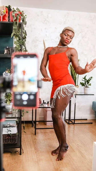 Kırmızı elbiseli, çıplak ayaklı Afro-Amerikalı, gündüz vakti oturma odasında sosyal medya için dans ediyor.