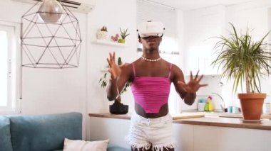 VR gözlüklü siyah bir transseksüel evdeki ışık odasında video oyunu oynarken siber uzayda nesnelere dokunuyor.