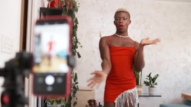 Afrika kökenli, kırmızı elbiseli, akıllı telefonun önünde dans eden, gündüz kuşağında blog için video kaydeden bir adam.