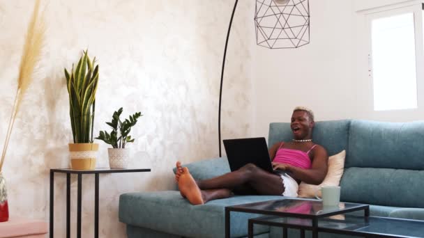 衣衫褴褛的非裔美国人在社交媒体上阅读惊人的新闻 在上网本键盘上打字 却坐在家里阳光灿烂的客厅里的沙发上 — 图库视频影像