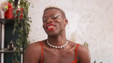 Neşeli Afrikalı Amerikalı travesti şık makyajlı kameraya bakıyor ve evinde gülüyor.