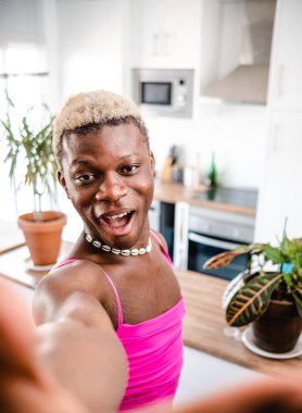 Modern mutfakta selfie çekerken gülümseyen ve kameraya bakan kısa saçlı Afro-Amerikan transseksüel erkek.