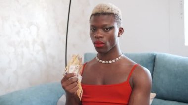 Elinde bir tomar avroluk banknotla siyahi Afrikalı adam evdeki kameraya ciddi ciddi bakıyor..