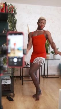 Evde video çekerken kırmızı elbiseli transseksüel siyah dansçı cep telefonunun önünde dans ediyor. Dikey video