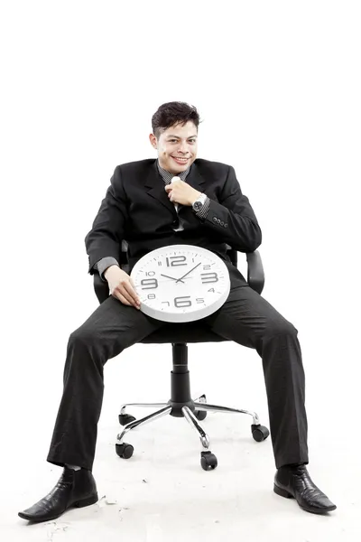 Portrait of a businessman sitting and put a clock between his leg against white background — Stock Photo, Image