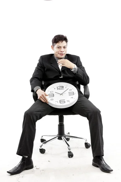 Porträtt av en affärsman som sitter och sätta en klocka mellan hans ben mot vit bakgrund — Stockfoto