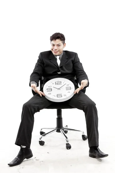 Portrait of a businessman sitting and put a clock between his leg against white background — Stock Photo, Image