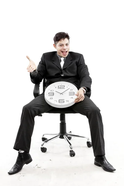 Portret van een zakenman zitten en zet een klok tussen zijn been tegen witte achtergrond — Stockfoto