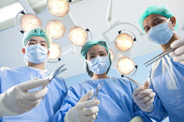 Debajo de la vista de cirujanos sosteniendo instrumentos médicos en las manos y mirando al paciente —  Fotos de Stock