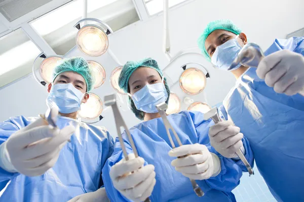 Abaixo a visão de cirurgiões segurando instrumentos médicos nas mãos e olhando para o paciente — Fotografia de Stock