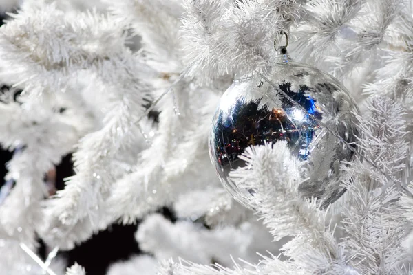 Un'immagine ravvicinata di una sfera ornamentale decorativa bianca di Natale su un ramo di abete bianco con l'illuminazione blu . — Foto Stock