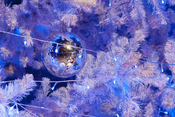 Eine Nahaufnahme einer weißen dekorativen Weihnachtskugel auf einem Tannenzweig mit blauer Beleuchtung. — Stockfoto