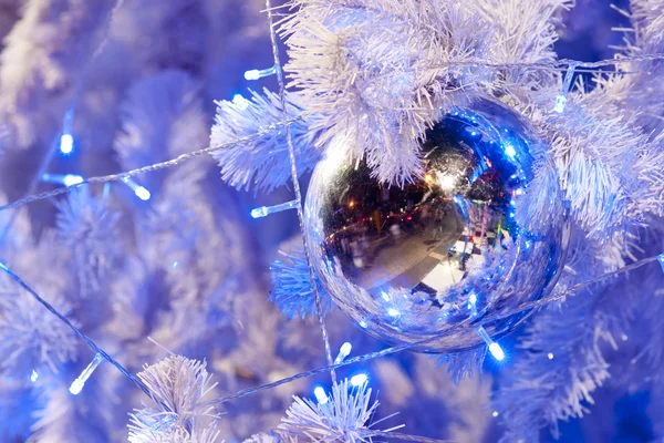 Крупный план белого декоративного рождественского шара на ветке белой елки с синим освещением . — стоковое фото