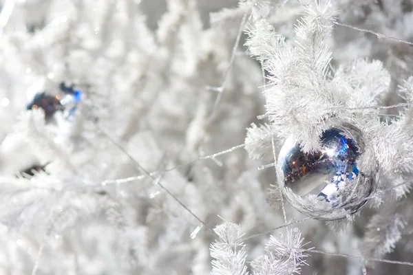 A close up image of a white decorative Christmas ornamental orb on a white fir tree branch with the blue lighting. — Stock Photo, Image