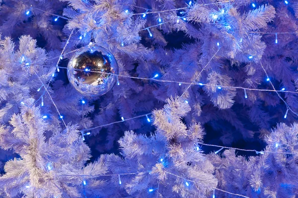 Eine Nahaufnahme einer weißen dekorativen Weihnachtskugel auf einem Tannenzweig mit blauer Beleuchtung. — Stockfoto