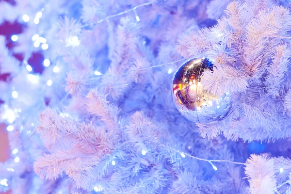 Un'immagine ravvicinata di una sfera ornamentale decorativa bianca di Natale su un ramo di abete bianco con l'illuminazione blu . — Foto Stock