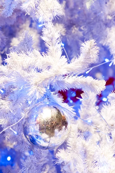 Una imagen de cerca de un orbe ornamental de Navidad decorativo blanco en una rama de abeto blanco con la iluminación azul . —  Fotos de Stock