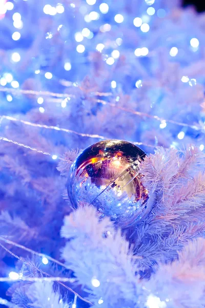 En närbild bild av en vit dekorativ jul prydnads klot på en vit Gran trädgren med blå belysning. — Stockfoto