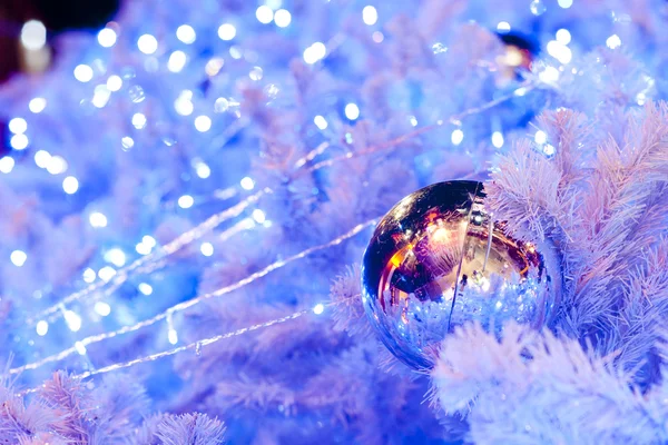 Eine Nahaufnahme einer weißen dekorativen Weihnachtskugel auf einem Tannenzweig mit blauer Beleuchtung. — Stockfoto