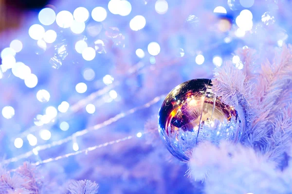 Un'immagine ravvicinata di una sfera ornamentale decorativa bianca di Natale su un ramo di abete bianco con l'illuminazione blu . — Foto Stock