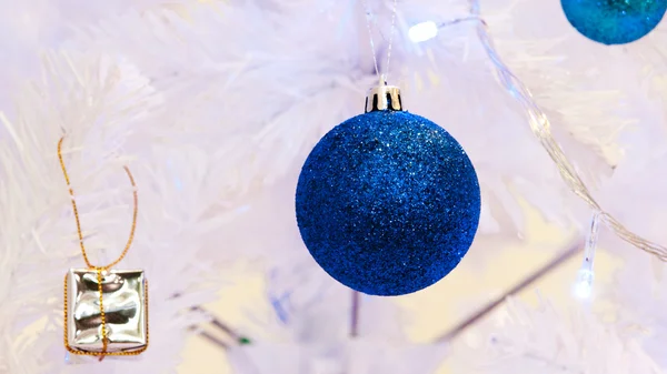 Eine Nahaufnahme einer weißen dekorativen Weihnachtskugel auf einem Tannenzweig mit blauer Beleuchtung. — Stockfoto