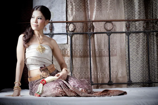 Wunderschöne asiatische Frau in thai Kleid liegend auf Bett — Stockfoto
