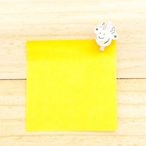 Yellow blank paper with the clip on the wooden background — Stock Photo, Image