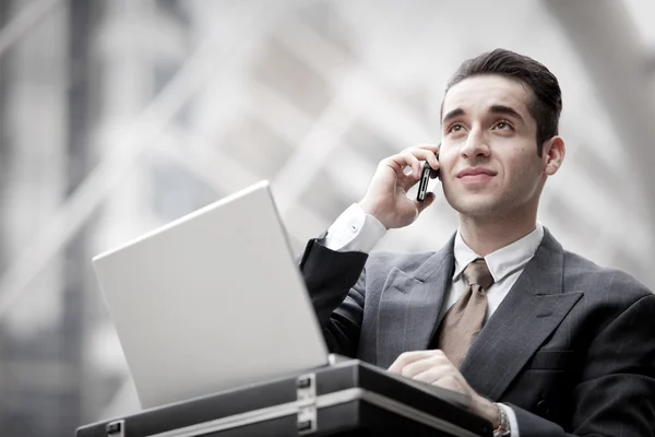 Knappe zakenman gelet telefoongesprek en met behulp van laptop — Stockfoto