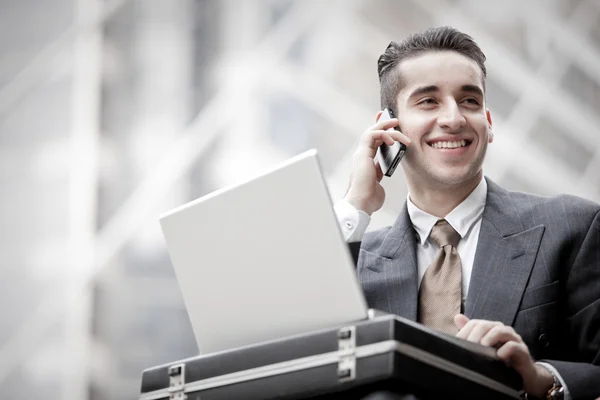 Hombre de negocios guapo que tiene llamada telefónica y el uso de ordenador portátil — Foto de Stock