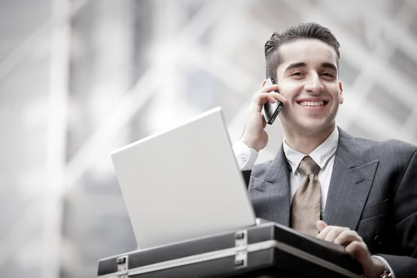 Hombre de negocios guapo que tiene llamada telefónica y el uso de ordenador portátil — Foto de Stock